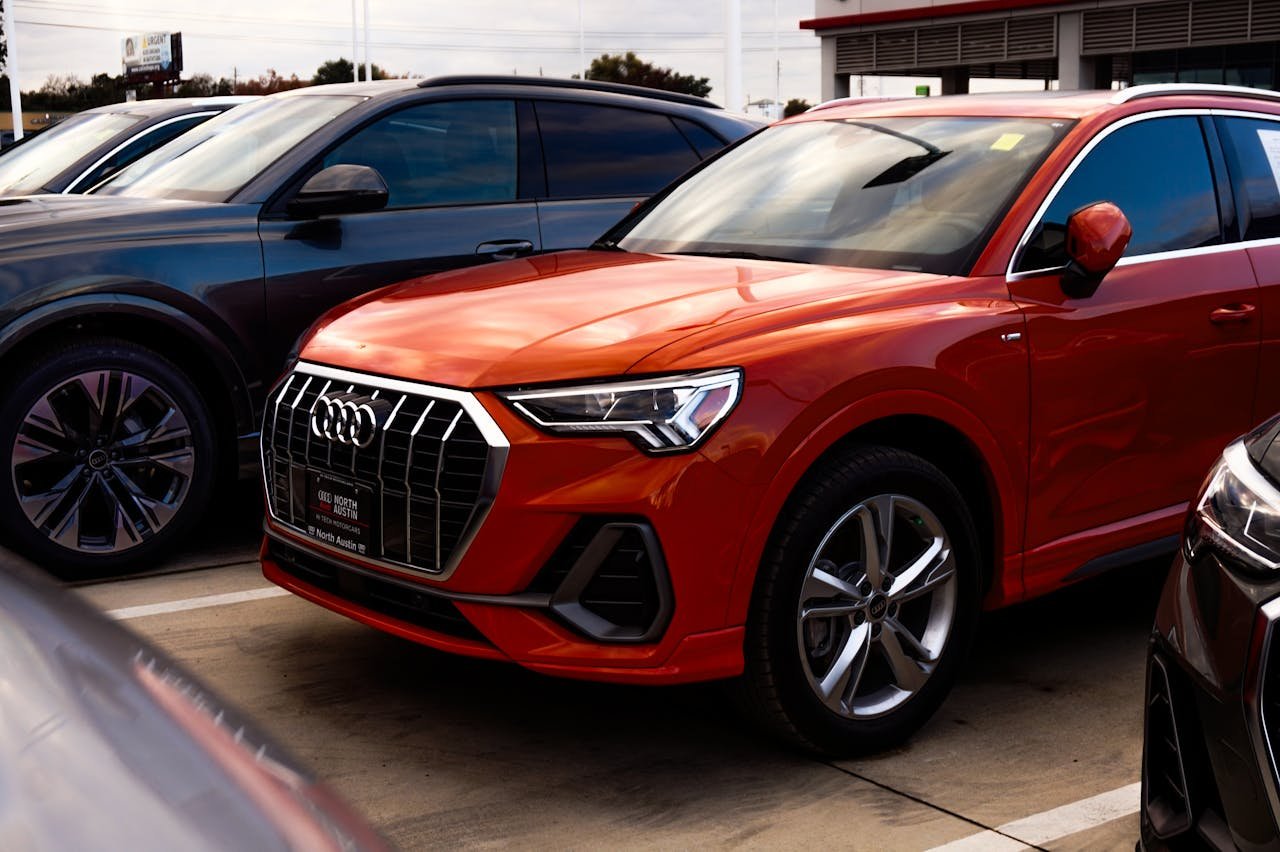 A vibrant orange SUV parked among other vehicles at a car dealership, showcasing modern car design.
