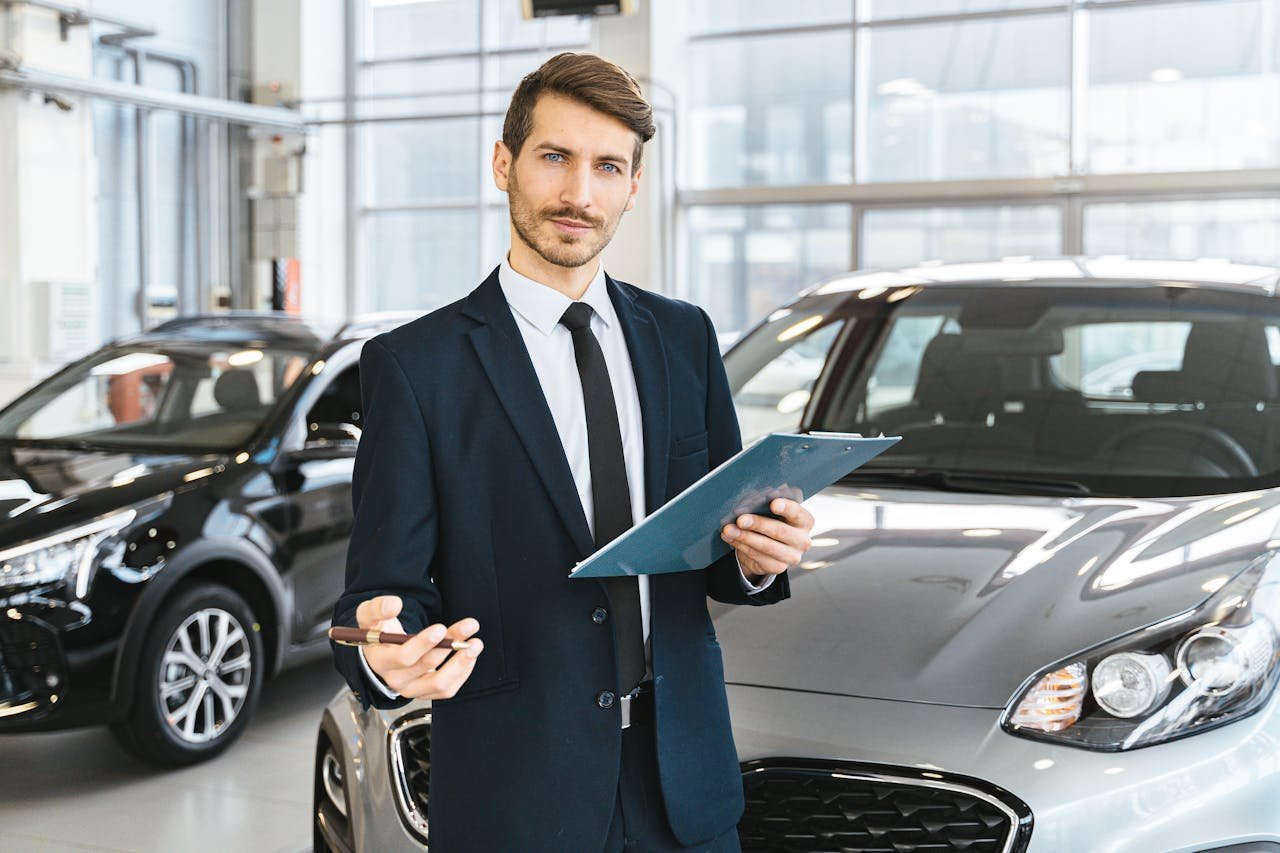 Professional car dealer in business suit holding clipboard in a bright car showroom.